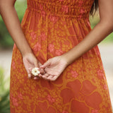 woman with brown hair wearing an orange long maxi dress with smocked bodice and spaghetti straps with puakenikeni print