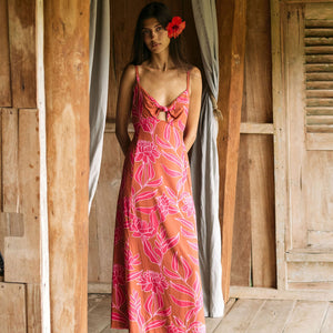 A woman with dark hair wears a YIREH full length dress featuring a knotted, sweetheart neckline. It is the Marina Dress in the Garden 'Awapuhi print. 