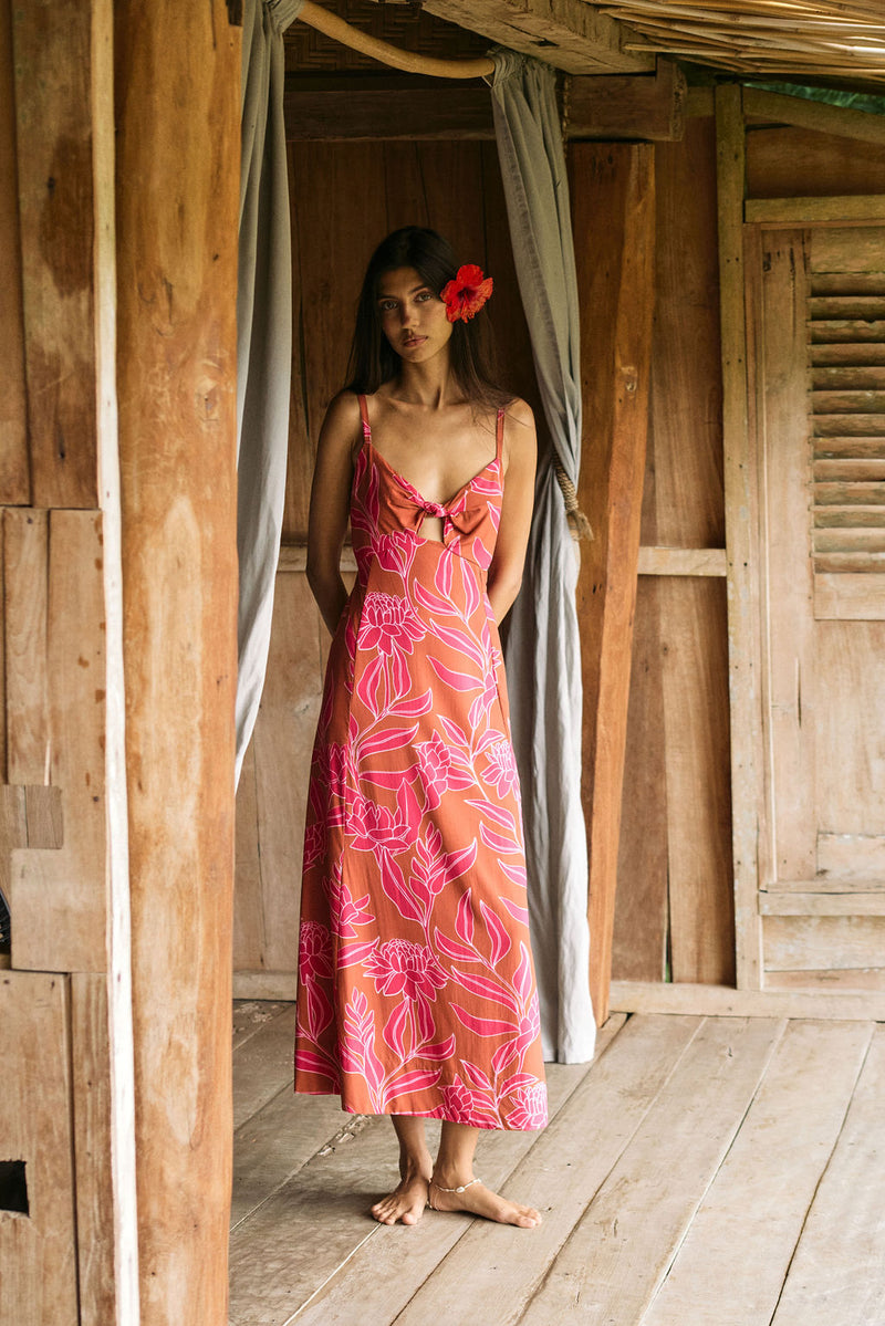 A woman with dark hair wears a YIREH full length dress featuring a knotted, sweetheart neckline. It is the Marina Dress in the Garden 'Awapuhi print. 