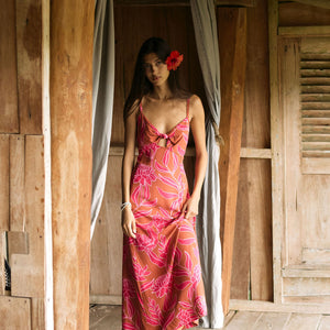 A woman with dark hair wears a YIREH full length dress featuring a knotted, sweetheart neckline. It is the Marina Dress in the Garden 'Awapuhi print. 