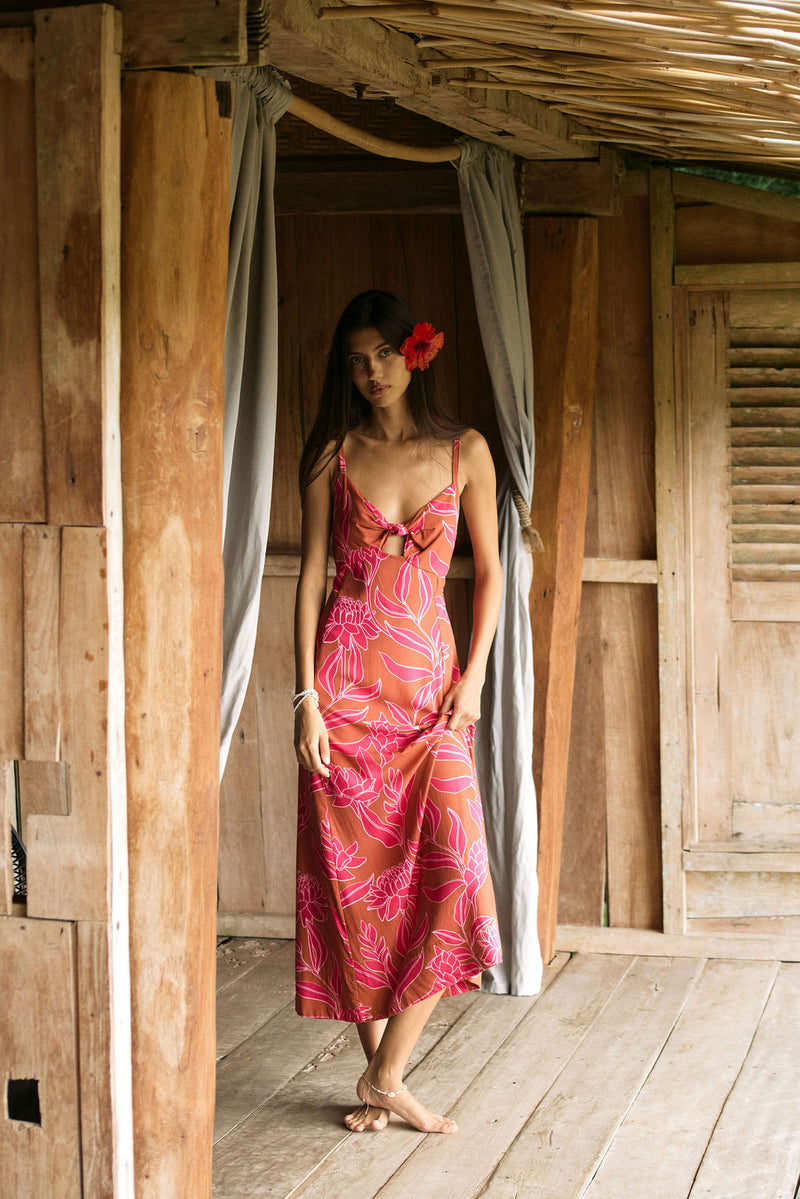 A woman with dark hair wears a YIREH full length dress featuring a knotted, sweetheart neckline. It is the Marina Dress in the Garden 'Awapuhi print. 