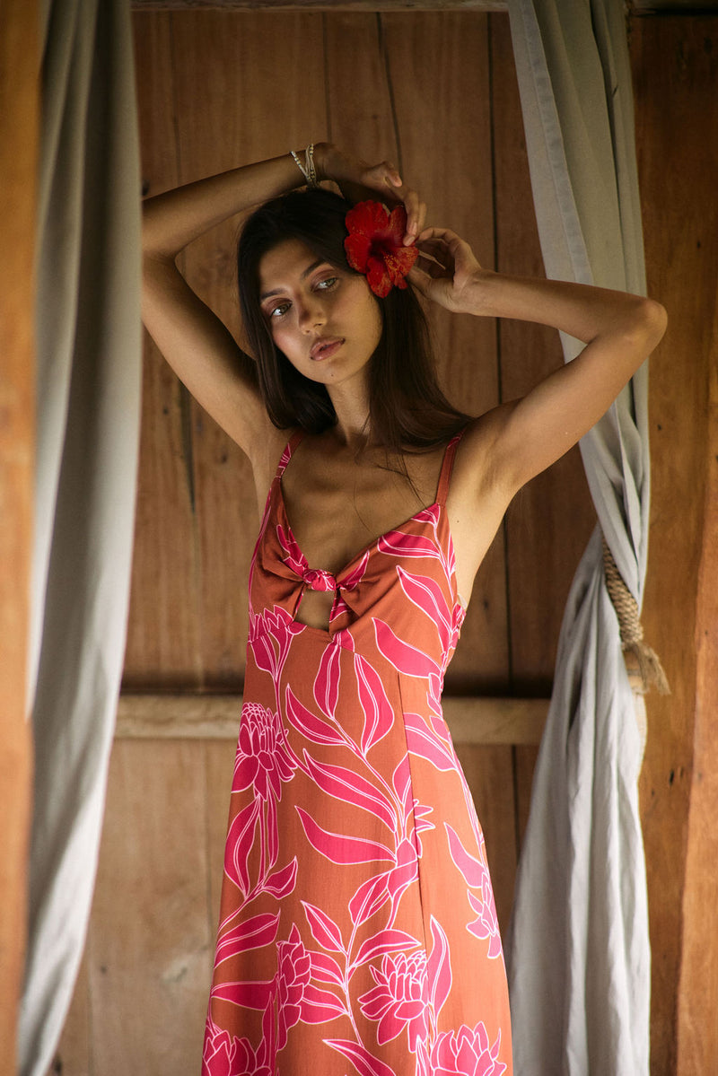 A woman with dark hair wears a YIREH full length dress featuring a knotted, sweetheart neckline. It is the Marina Dress in the Garden 'Awapuhi print. 