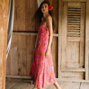 A woman with dark hair wears a YIREH full length dress featuring a knotted, sweetheart neckline. It is the Marina Dress in the Garden 'Awapuhi print. 
