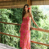 A woman with dark hair wears a YIREH full length dress featuring a knotted, sweetheart neckline. It is the Marina Dress in the Garden 'Awapuhi print. 