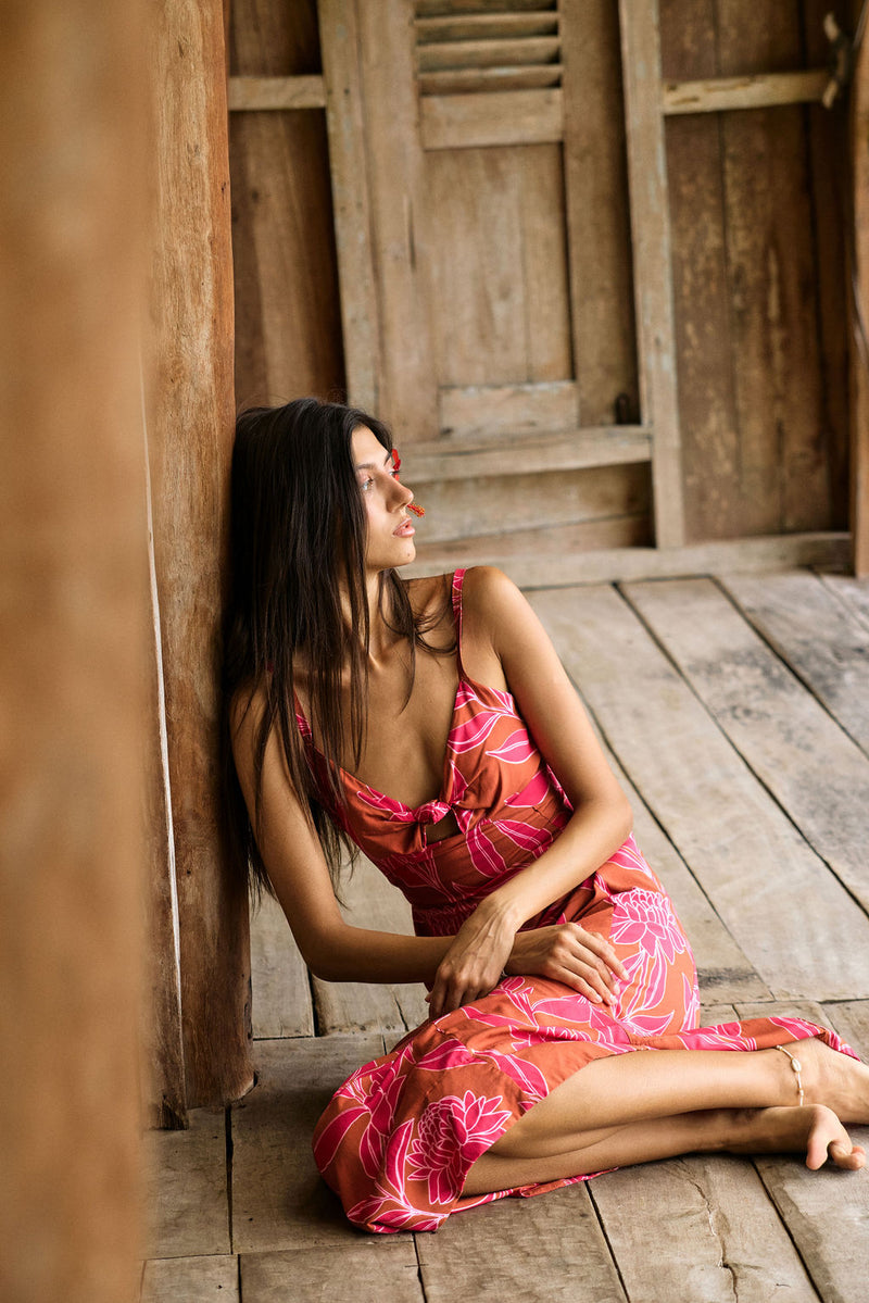 A woman with dark hair wears a YIREH full length dress featuring a knotted, sweetheart neckline. It is the Marina Dress in the Garden 'Awapuhi print. 