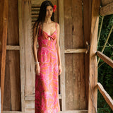 A woman with dark hair wears a YIREH full length dress featuring a knotted, sweetheart neckline. It is the Marina Dress in the Garden 'Awapuhi print. 