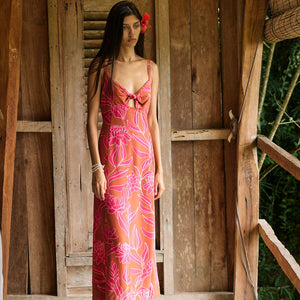 A woman with dark hair wears a YIREH full length dress featuring a knotted, sweetheart neckline. It is the Marina Dress in the Garden 'Awapuhi print. 