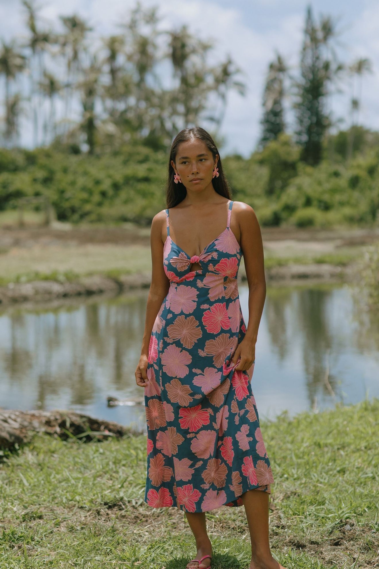 woman with brown hair wearing a navy maxi dress with knot neckline and bright pink hibiscus print