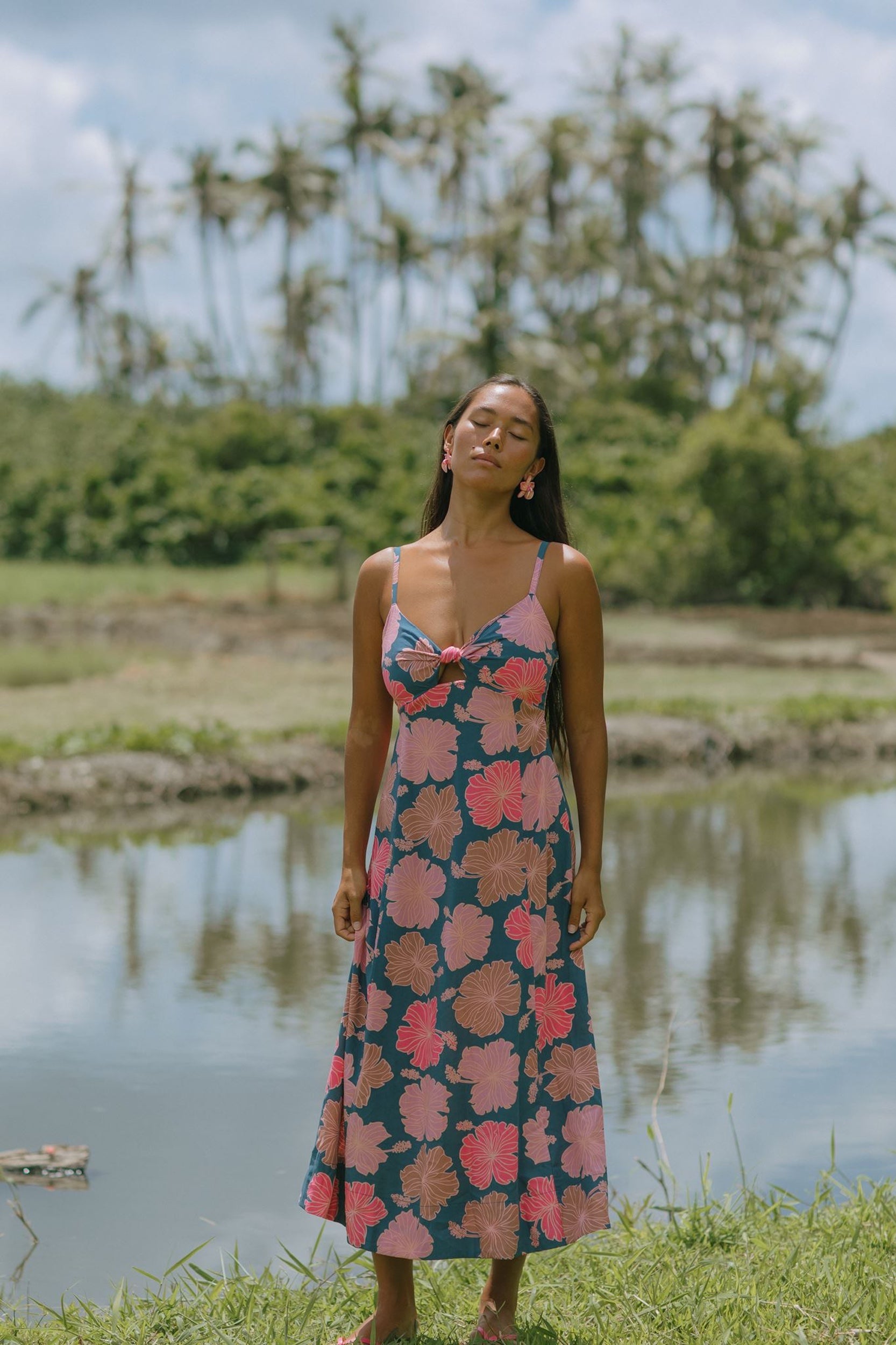 woman with brown hair wearing a navy maxi dress with knot neckline and bright pink hibiscus print