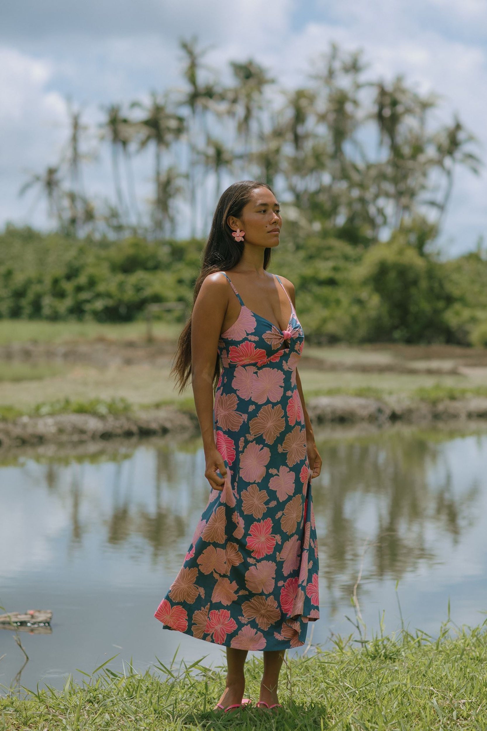 woman with brown hair wearing a navy maxi dress with knot neckline and bright pink hibiscus print