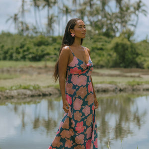 woman with brown hair wearing a navy maxi dress with knot neckline and bright pink hibiscus print