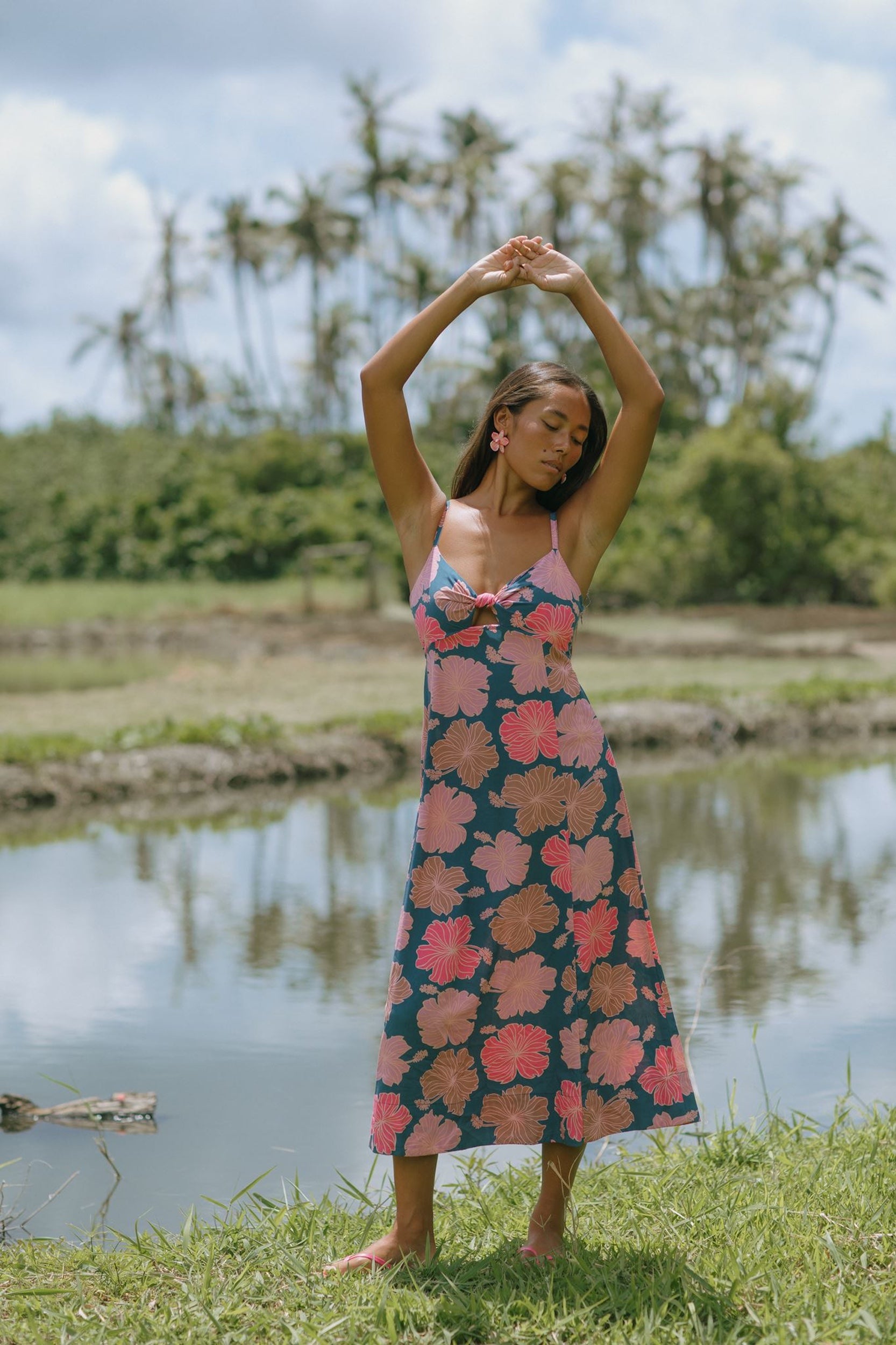 woman with brown hair wearing a navy maxi dress with knot neckline and bright pink hibiscus print