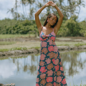 woman with brown hair wearing a navy maxi dress with knot neckline and bright pink hibiscus print