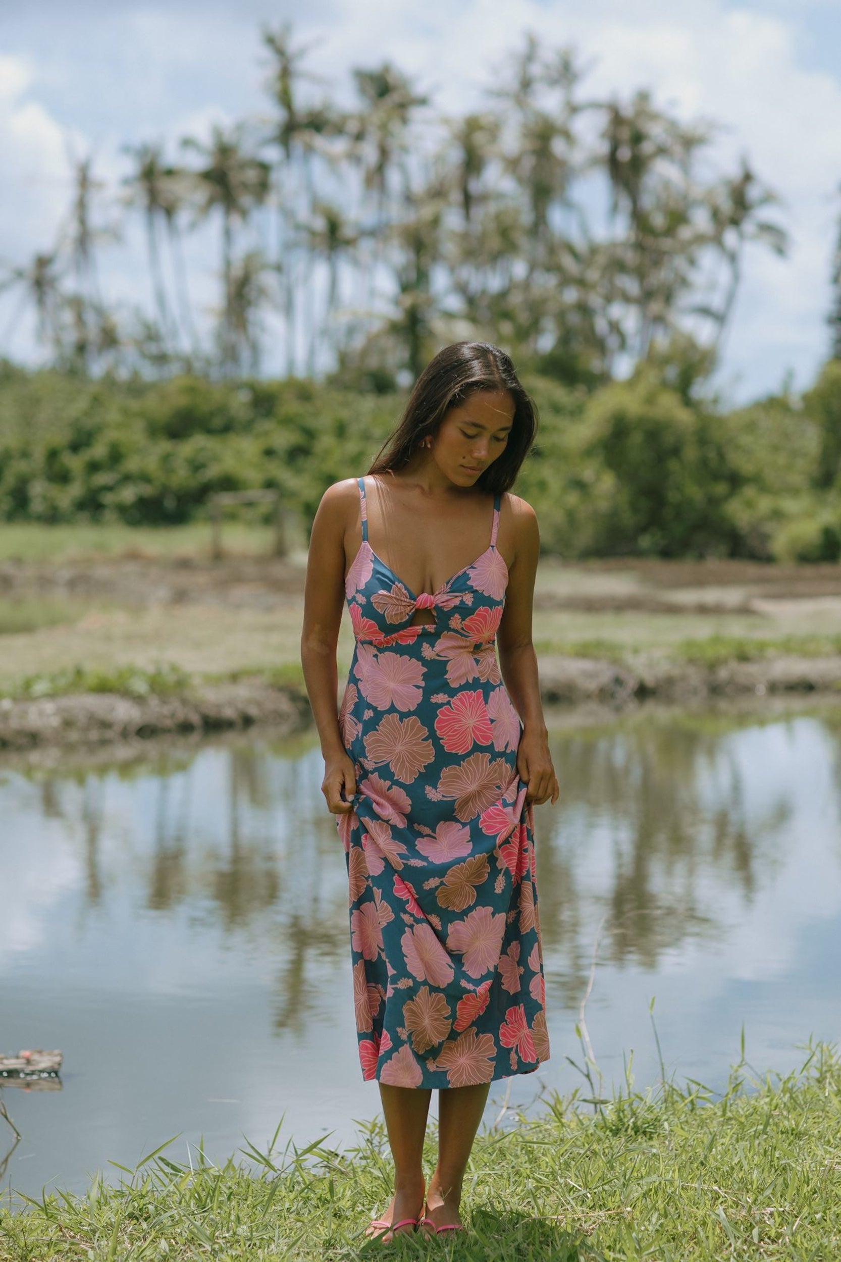 woman with brown hair wearing a navy maxi dress with knot neckline and bright pink hibiscus print