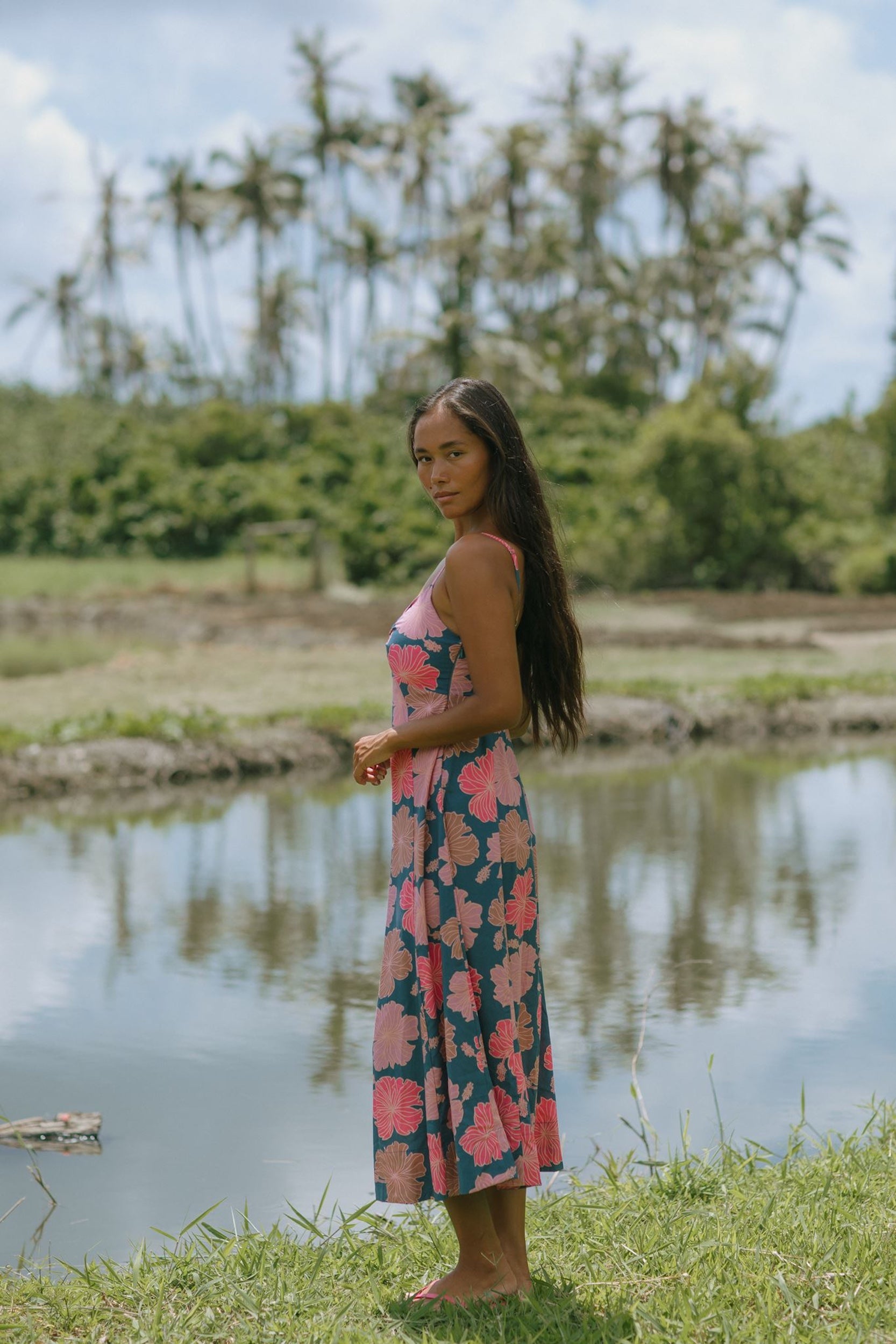 woman with brown hair wearing a navy maxi dress with knot neckline and bright pink hibiscus print