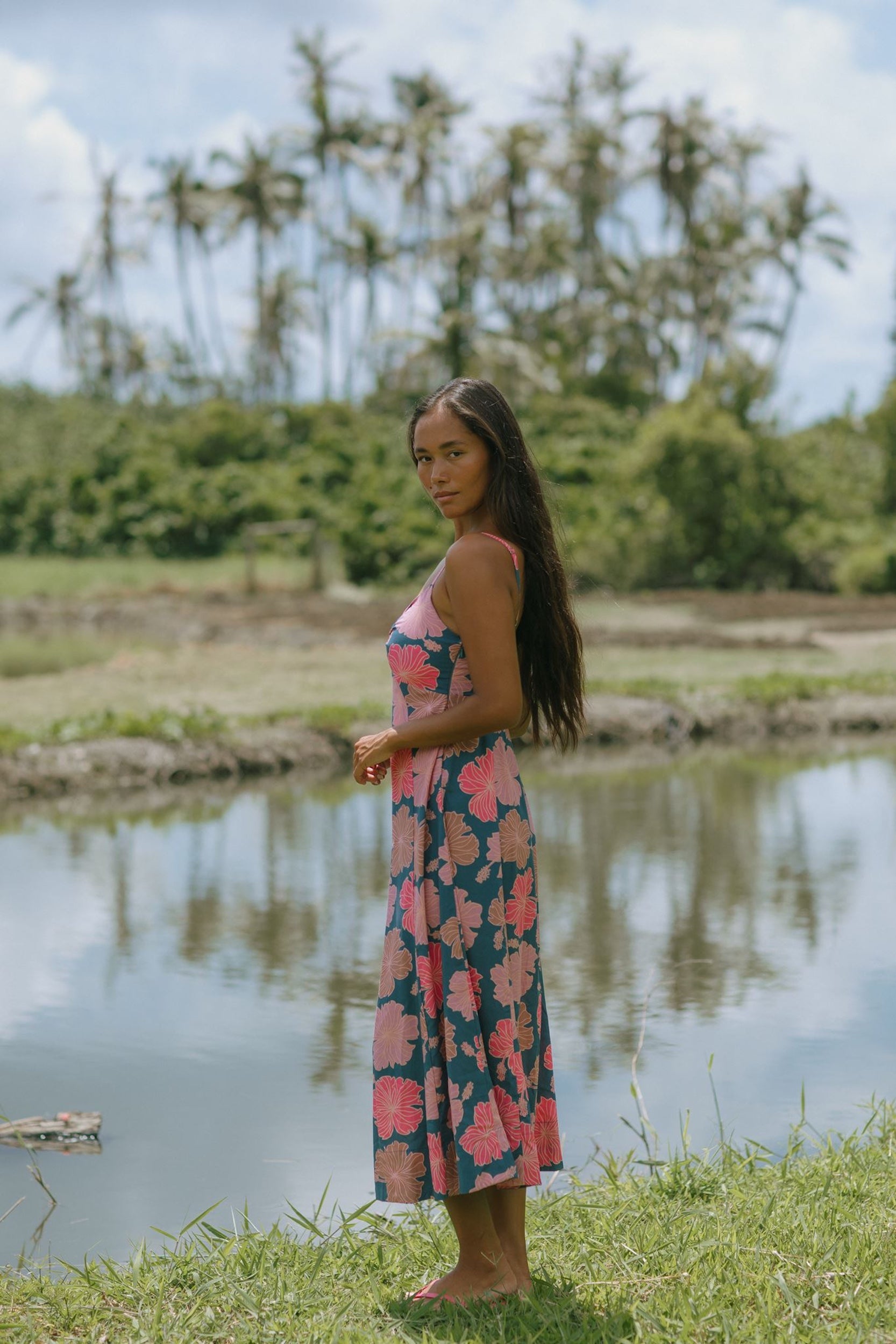 woman with brown hair wearing a navy maxi dress with knot neckline and bright pink hibiscus print