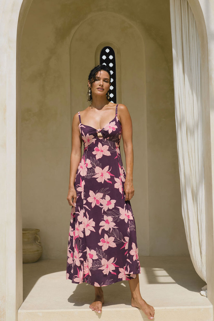 woman with brown hair wearing a dark purple maxi dress with knot tie front and orchid pattern