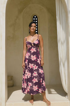 woman with brown hair wearing a dark purple maxi dress with knot tie front and orchid pattern
