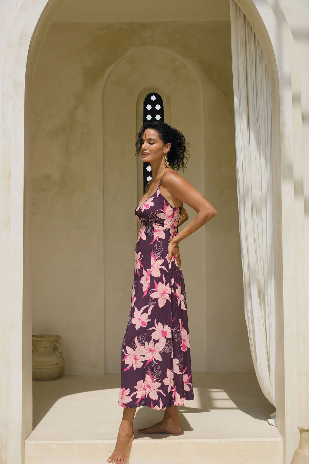 woman with brown hair wearing a dark purple maxi dress with knot tie front and orchid pattern