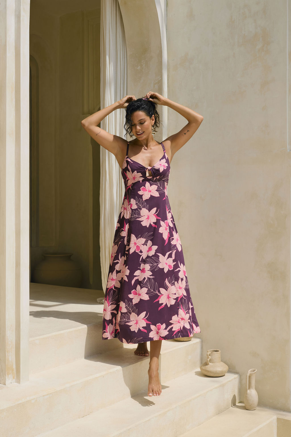 woman with brown hair wearing a dark purple maxi dress with knot tie front and orchid pattern