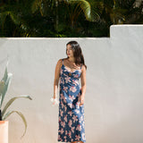 woman with black hair wearing a maxi dress with knot cutout neckline in a navy and pink hibiscus print. 