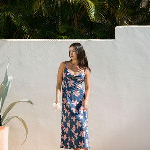 woman with black hair wearing a maxi dress with knot cutout neckline in a navy and pink hibiscus print. 
