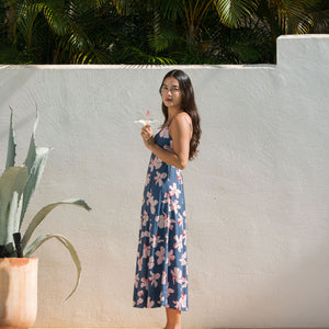 woman with black hair wearing a maxi dress with knot cutout neckline in a navy and pink hibiscus print. 
