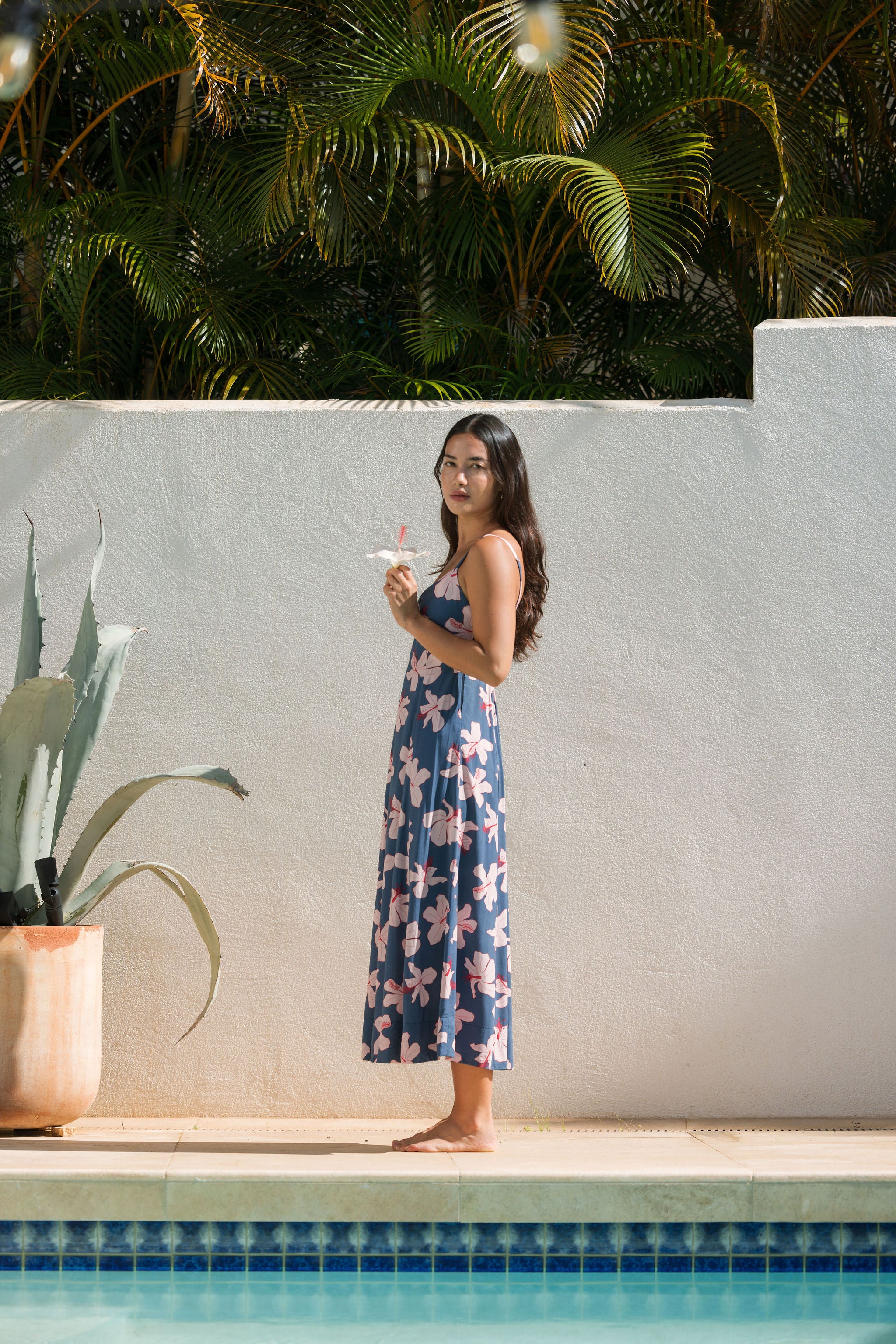woman with black hair wearing a maxi dress with knot cutout neckline in a navy and pink hibiscus print. 