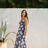 woman with black hair wearing a maxi dress with knot cutout neckline in a navy and pink hibiscus print. 
