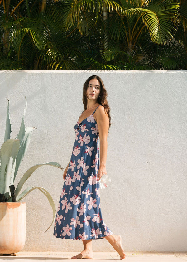 woman with black hair wearing a maxi dress with knot cutout neckline in a navy and pink hibiscus print. 