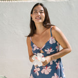 woman with black hair wearing a maxi dress with knot cutout neckline in a navy and pink hibiscus print. 