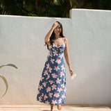 woman with black hair wearing a maxi dress with knot cutout neckline in a navy and pink hibiscus print. 