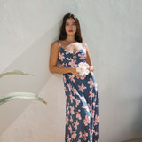 woman with black hair wearing a maxi dress with knot cutout neckline in a navy and pink hibiscus print. 