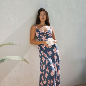 woman with black hair wearing a maxi dress with knot cutout neckline in a navy and pink hibiscus print. 