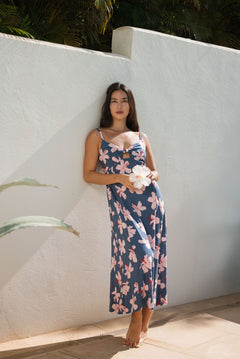 woman with black hair wearing a maxi dress with knot cutout neckline in a navy and pink hibiscus print. 
