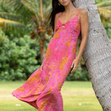 woman wearing a pink spaghetti strap maxi dress with a knot bust with lei print
