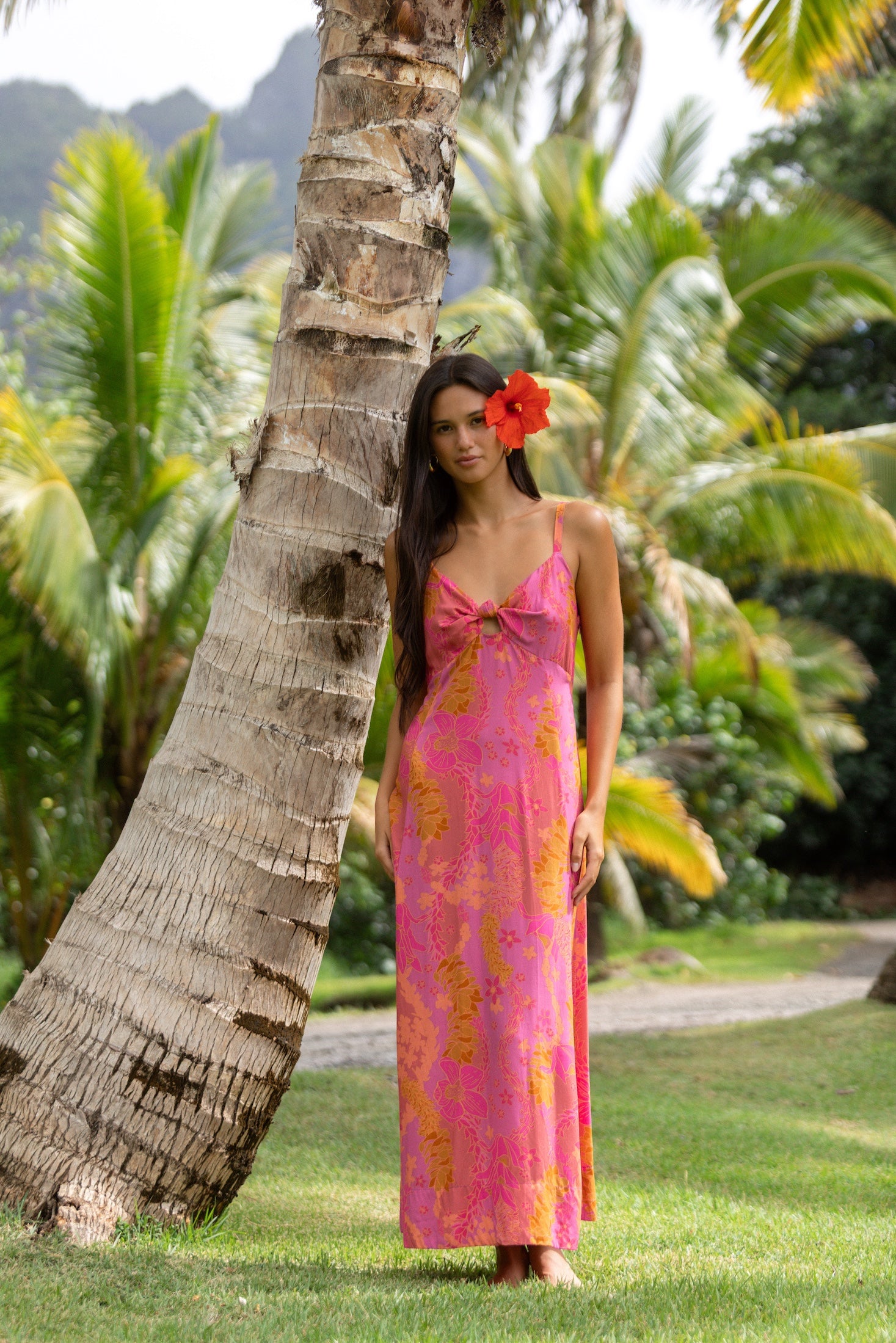 woman wearing a pink spaghetti strap maxi dress with a knot bust with lei print