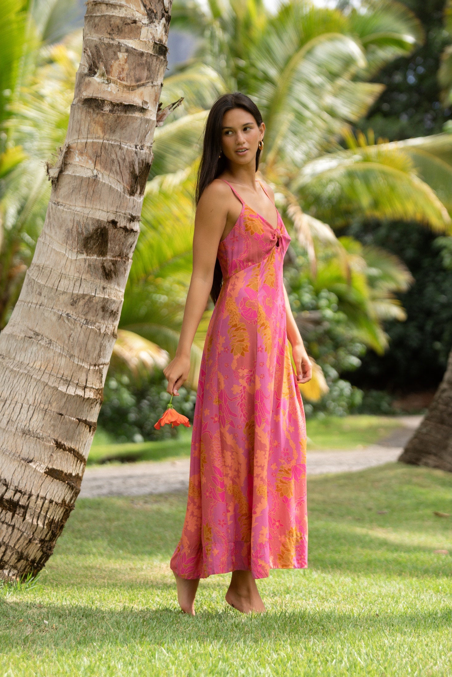 woman wearing a pink spaghetti strap maxi dress with a knot bust with lei print