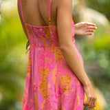 woman wearing a pink spaghetti strap maxi dress with a knot bust with lei print