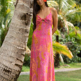 woman wearing a pink spaghetti strap maxi dress with a knot bust with lei print