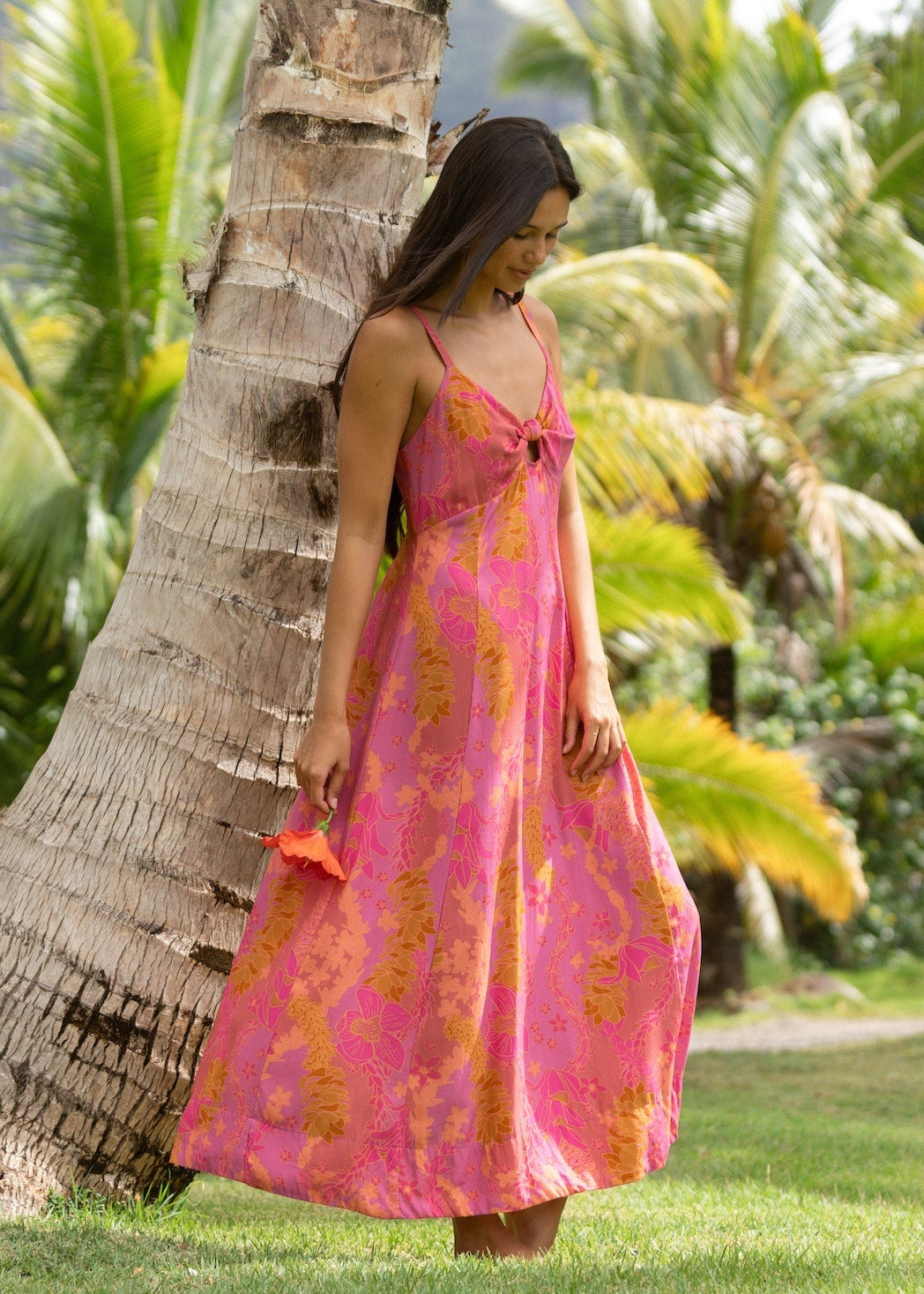 woman wearing a pink spaghetti strap maxi dress with a knot bust with lei print