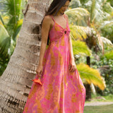 woman wearing a pink spaghetti strap maxi dress with a knot bust with lei print