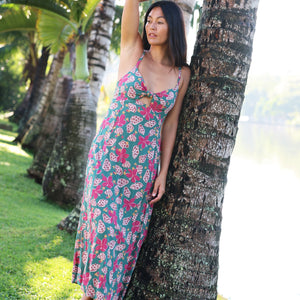 woman with brown hair wearing a teal maxi dress wth tie knot detail and shell and pua pattern