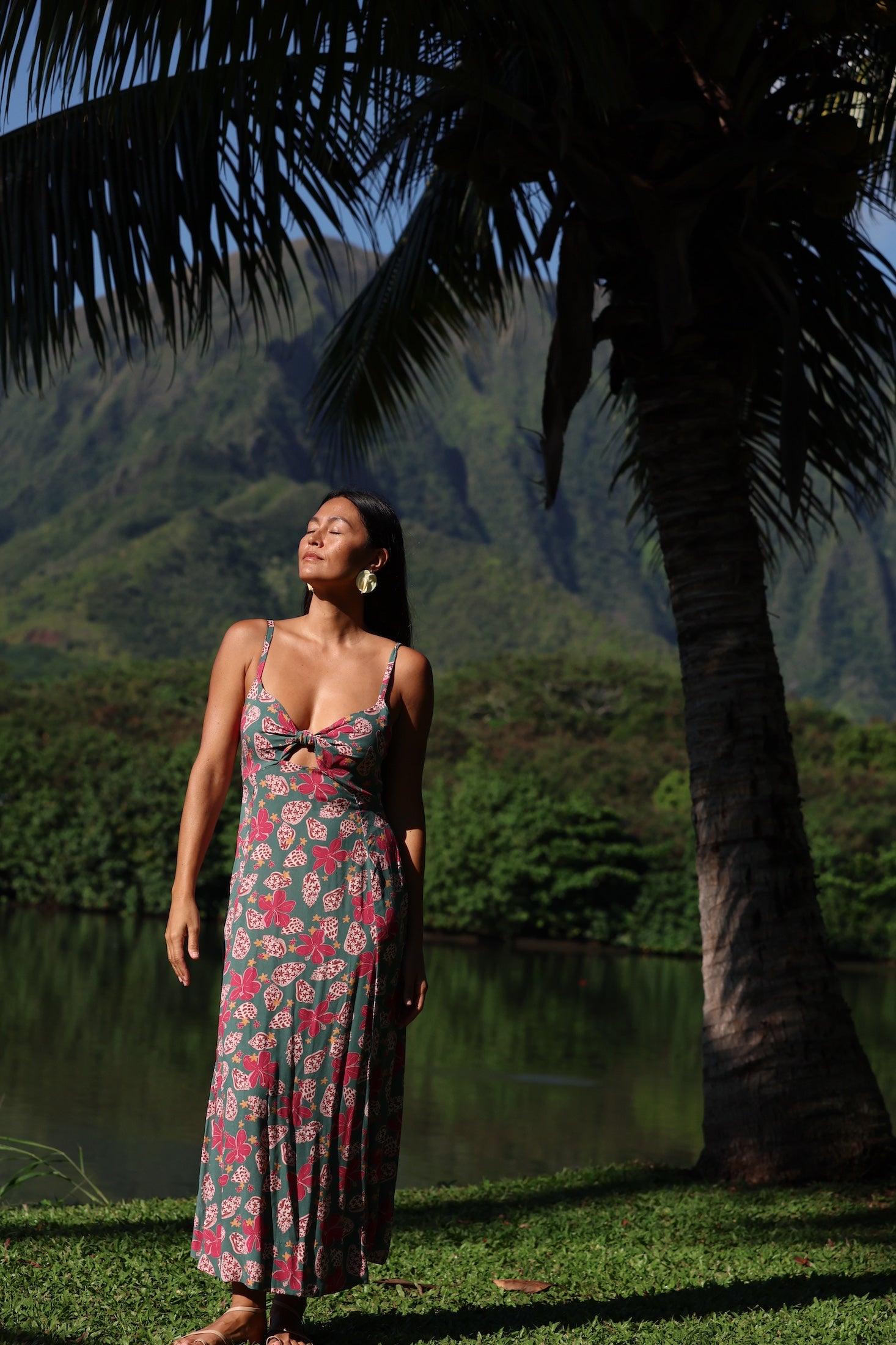 woman with brown hair wearing a teal maxi dress wth tie knot detail and shell and pua pattern
