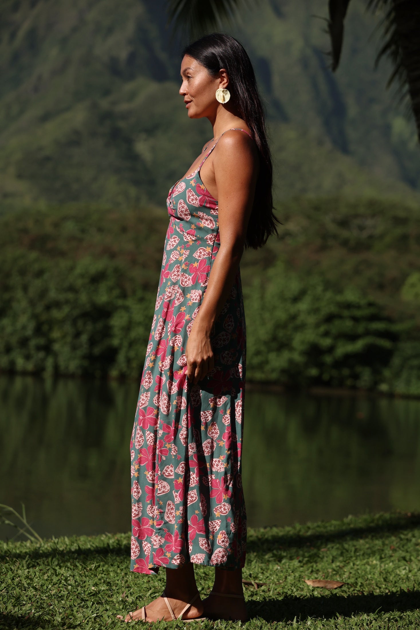 woman with brown hair wearing a teal maxi dress wth tie knot detail and shell and pua pattern