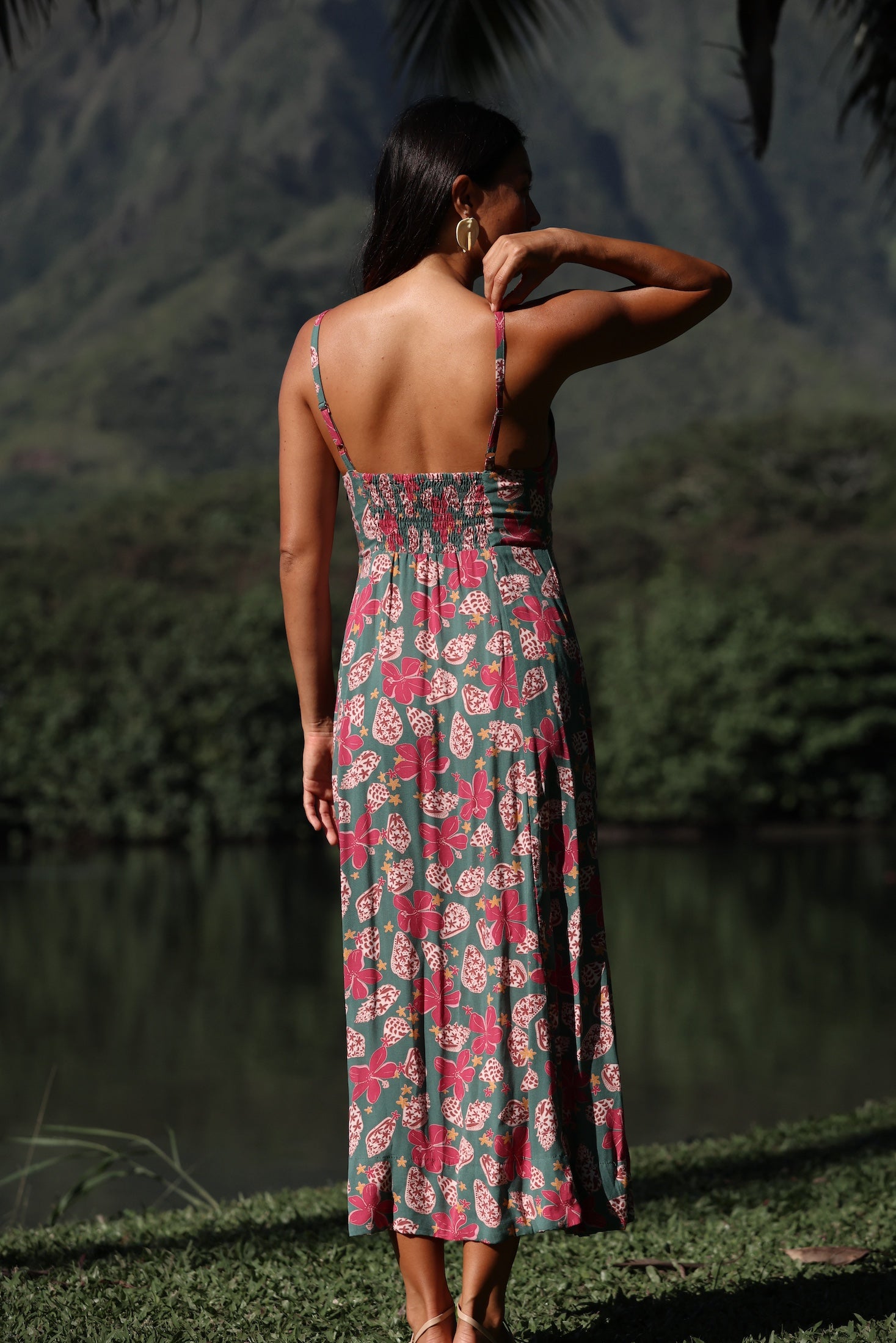 woman with brown hair wearing a teal maxi dress wth tie knot detail and shell and pua pattern