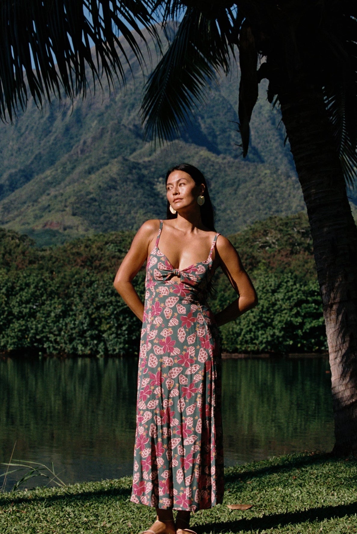 woman with brown hair wearing a teal maxi dress wth tie knot detail and shell and pua pattern
