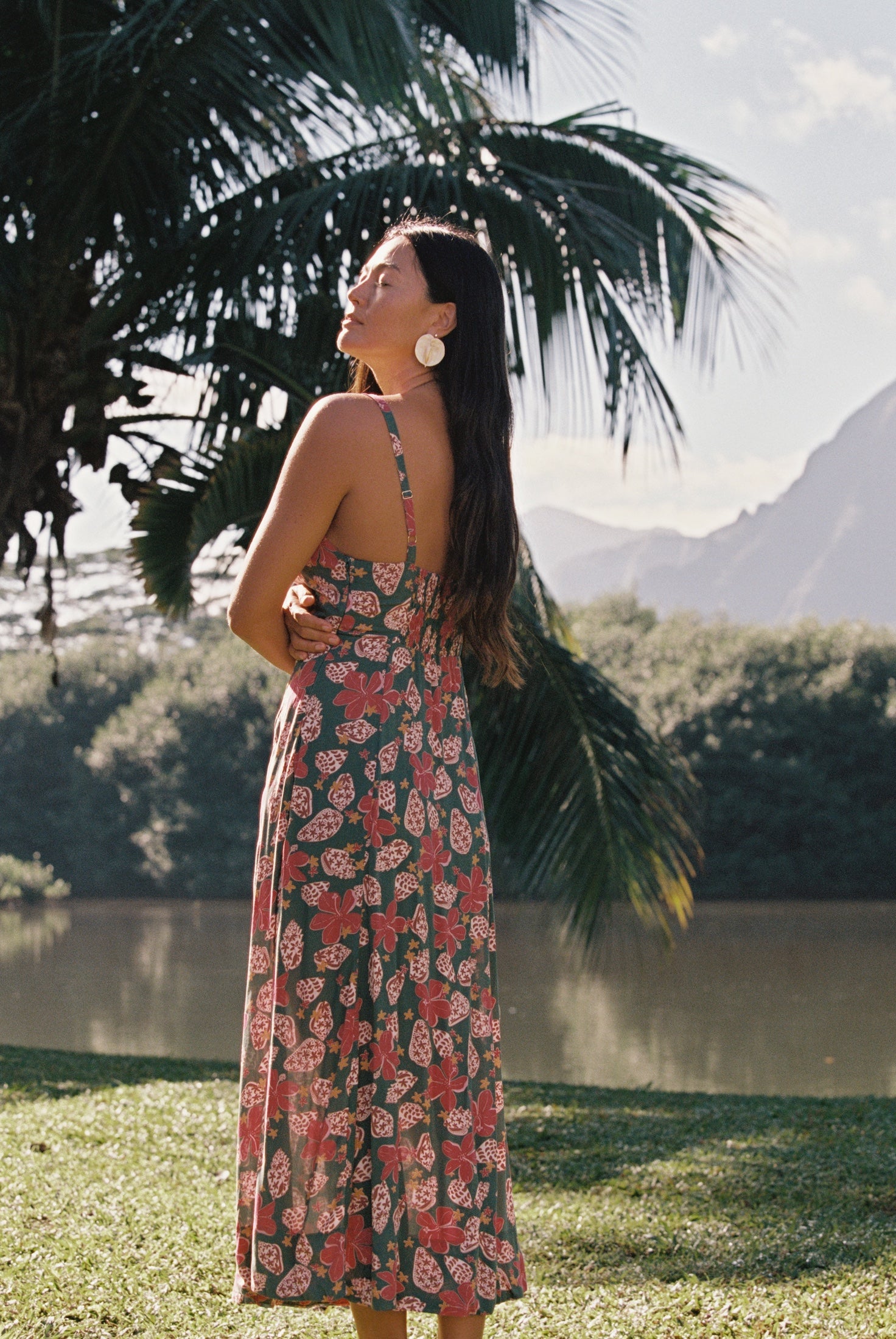 woman with brown hair wearing a teal maxi dress wth tie knot detail and shell and pua pattern