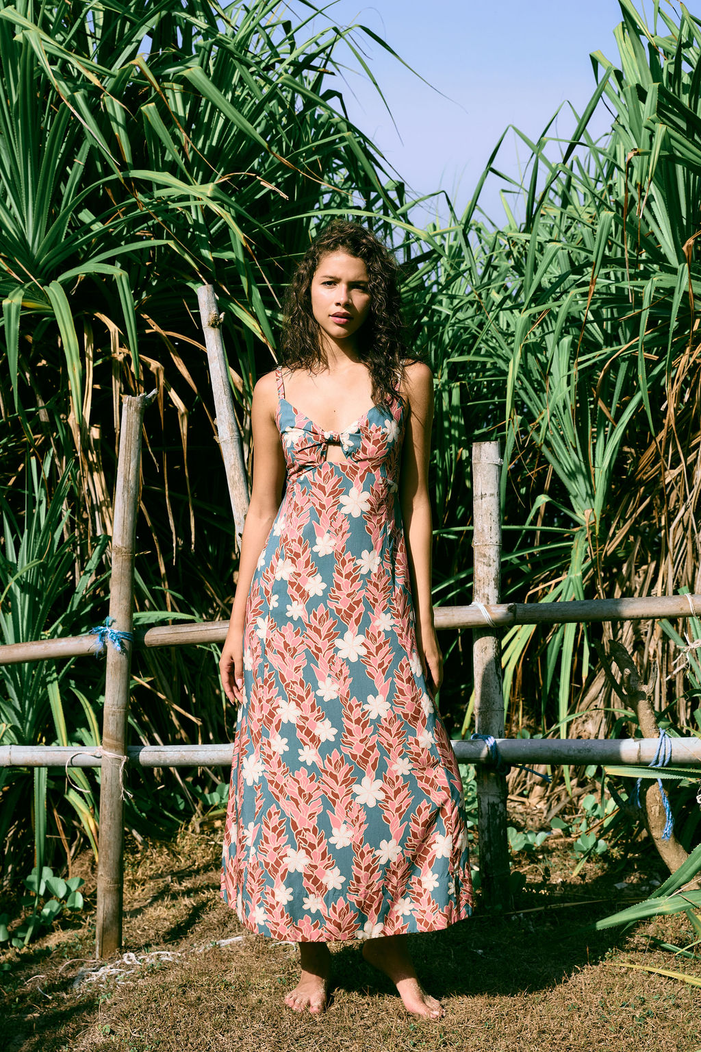 woman with brown hair wearing wearing a long maxi dress with knot tie neckline in a red ginger and tiare print