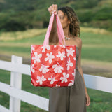 Woman with tote bag with beige and pink hibiscus print on orange red ground.
